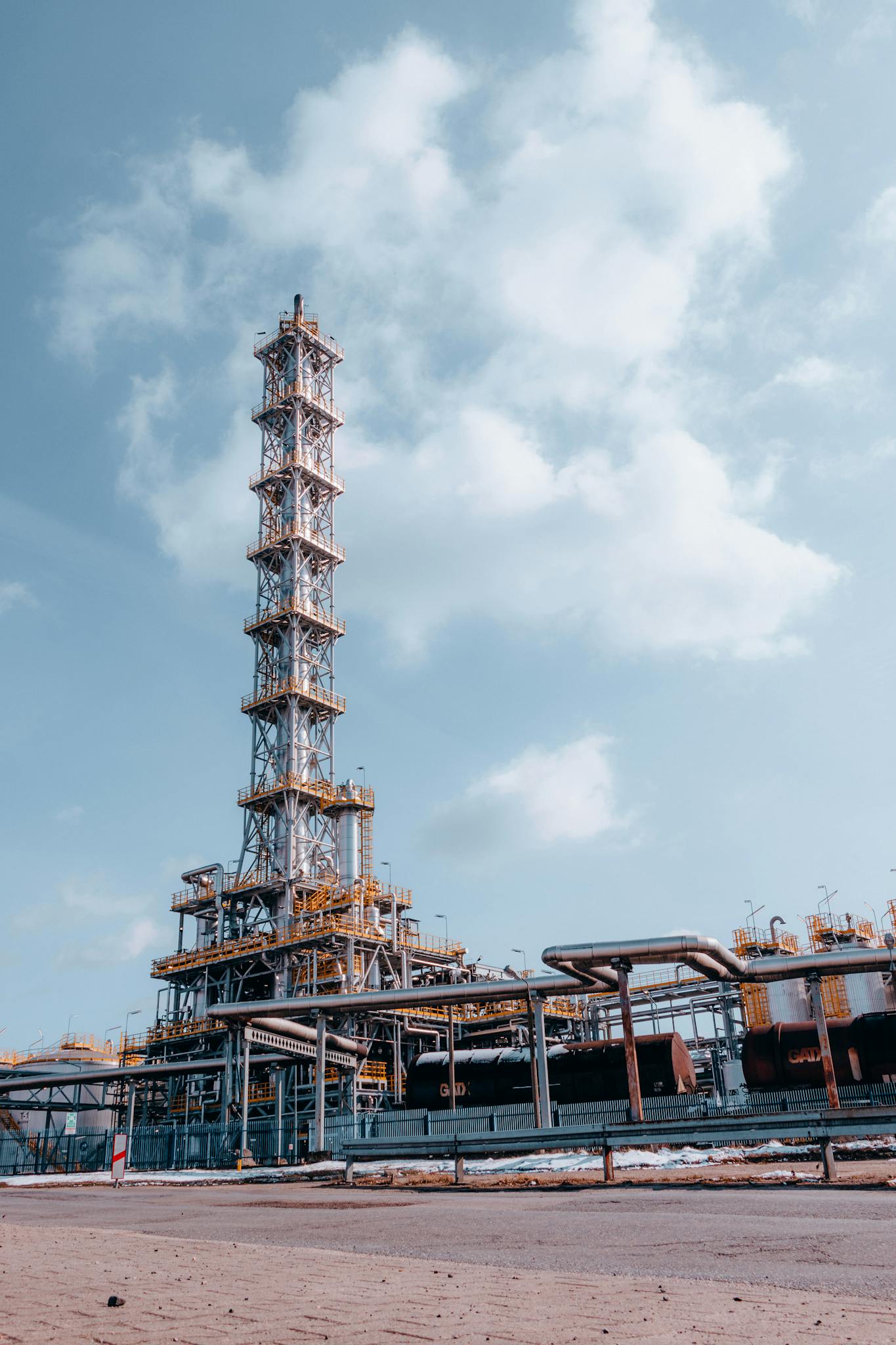 A vertical shot of an oil refinery tower in Trzebinia, showcasing industrial architecture against a blue sky.