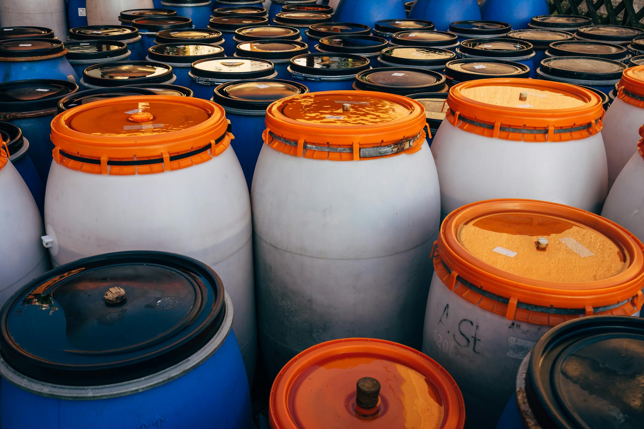 Close-up of blue and white plastic barrels with orange lids in storage area.